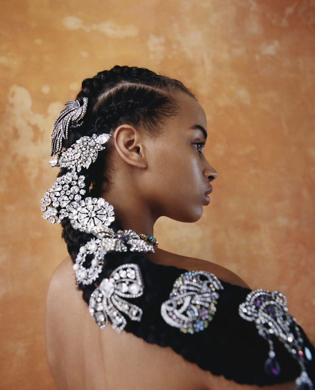 Profile shot of an African-American woman with braided hair adorned with sparkling jeweled hair accessories against an orange backdrop.