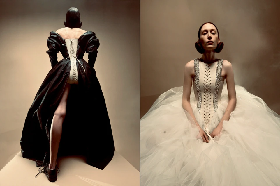 Two fashion models pose in contrasting gowns, one black and one white, in a studio setting with soft lighting, showcasing elegant design.