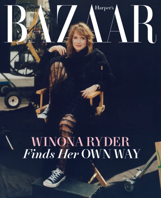Winona Ryder poses for a Harper's Bazaar cover in a black outfit and sneakers, seated in a director's chair amidst film equipment.