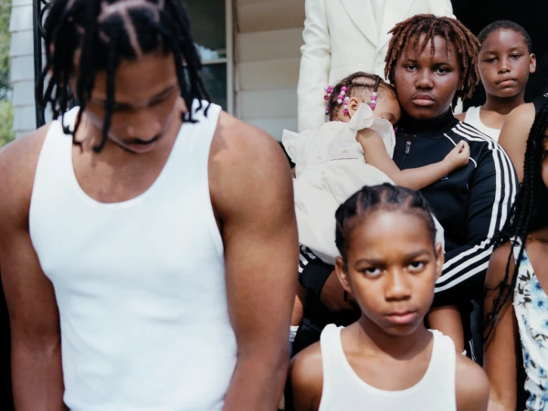 Group portrait of a Black family outdoors, featuring a man in a white tank top and a young boy with braided hair.