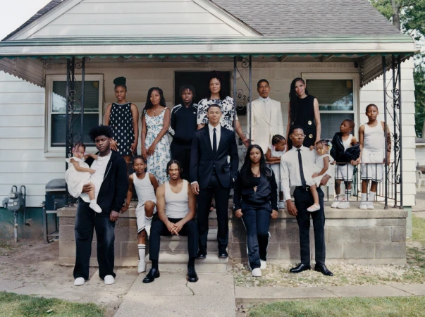 A large group of well-dressed African-American people stand and sit on the steps of a small house, posing for a family or group portrait.
