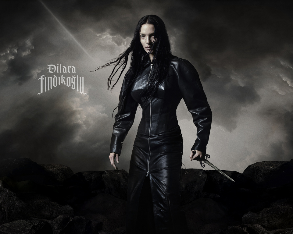 Portrait of a woman with long black hair, wearing a black leather outfit and holding a dagger, set against a stormy cloud background.