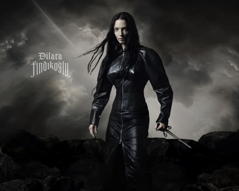 Portrait of a woman with long black hair, wearing a black leather outfit and holding a dagger, set against a stormy cloud background.