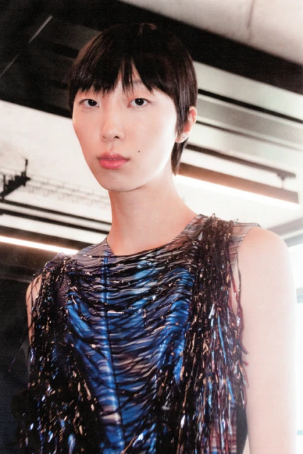 Close-up of a person with dark hair wearing a sleeveless top featuring a blue and black abstract design and fringe detail.
