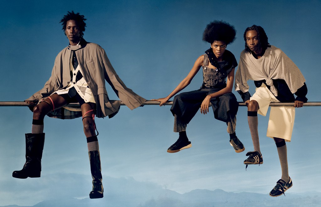 Three fashion models sit on a metal bar against a blue gradient background wearing clothes with a mix of textures and styles.