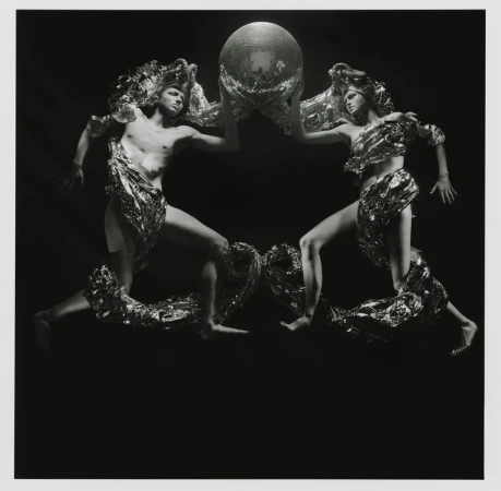 Two figures draped in metallic fabric hold a mirrored disco ball in a high-contrast black and white studio photography composition.