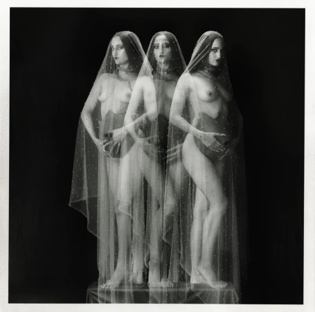 Three pregnant women stand in a dark studio. The women are partially obscured by a thin, spotted translucent veil. The photo is black and white.