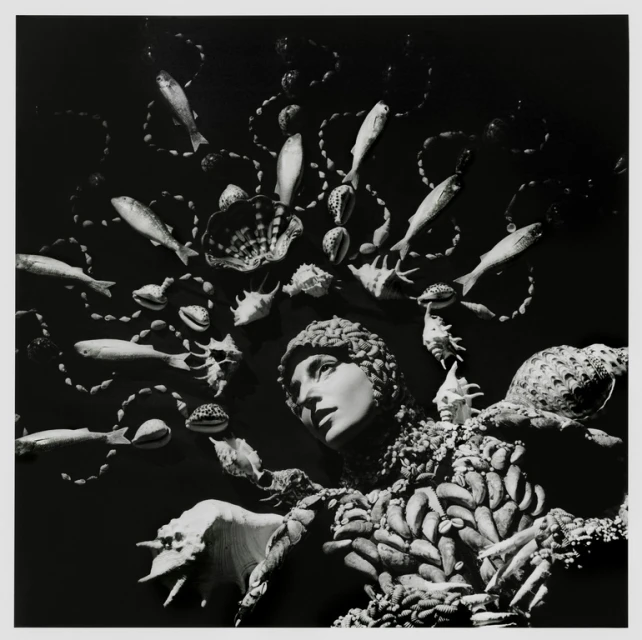 Monochrome portrait of a person adorned with seashells and fish, creating a surreal and artistic headpiece, set against a dark background.