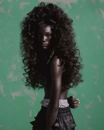 Black woman with voluminous curly hair wearing dark shorts against a textured green background, cast by Affa Osman.