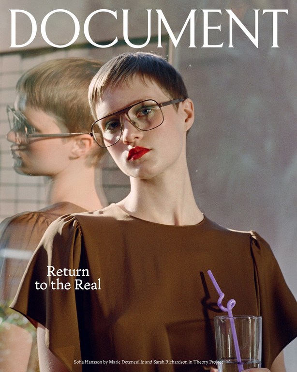 Close-up magazine cover shot of a young adult woman with short hair wearing glasses and a brown top, with a glass of water.