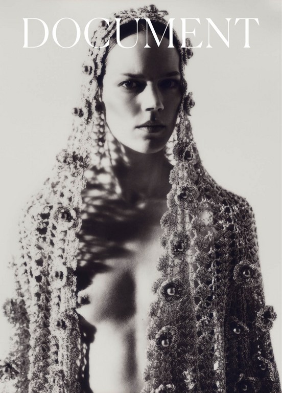 Black and white portrait of a woman with lace headdress and shawl posing in a photo studio with a bright background.