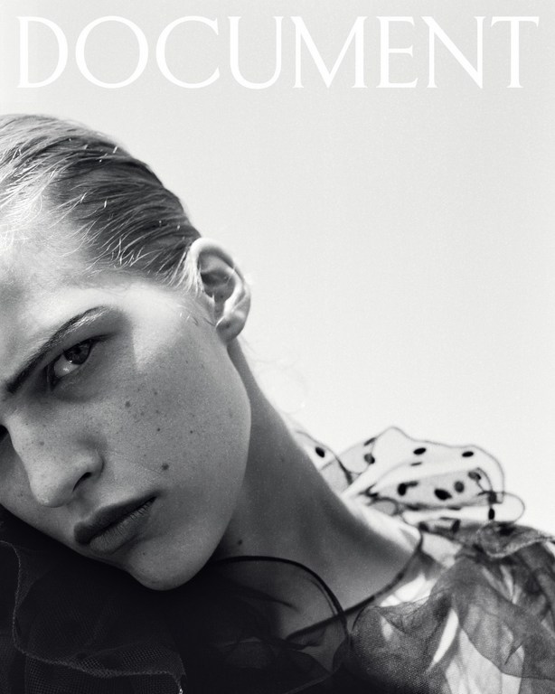 Close-up monochrome portrait of a model with slicked-back hair wearing a sheer polka-dot ruffled collar.
