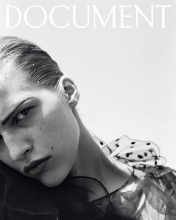 Close-up monochrome portrait of a model with slicked-back hair wearing a sheer polka-dot ruffled collar.