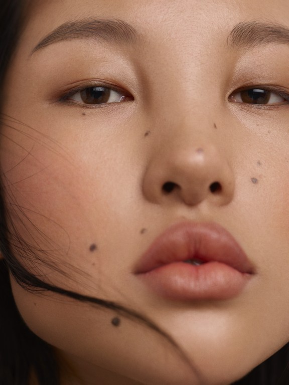 Close-up of an Asian woman's face in a beauty shot with fair skin, brown eyes, and full lips, showcasing a minimalist aesthetic.