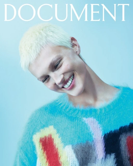 Magazine cover featuring a smiling person with short blonde hair wearing a colorful sweater against a light blue background.