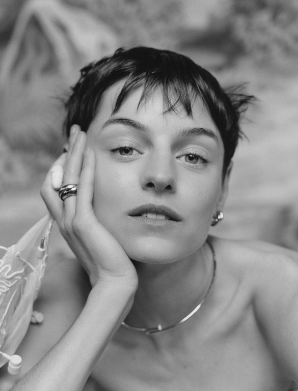 Close-up portrait of a woman with short dark hair resting her chin on her hand, wearing a thin necklace and rings, by Miguel Bento.