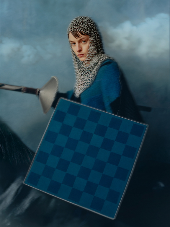 Person in a chainmail coif poses in a stylized shot with a chessboard-patterned shield and sword, set against a cloudy backdrop.