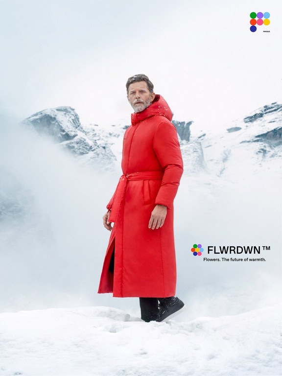 A mature man models a red puffer coat with a belt against a snowy mountain backdrop, showcasing winter fashion in a minimalist style.