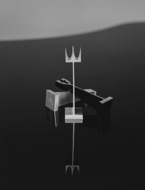 Abstract composition featuring a trident-like object and geometric shapes in a monochrome color palette, reflecting on a shiny surface.