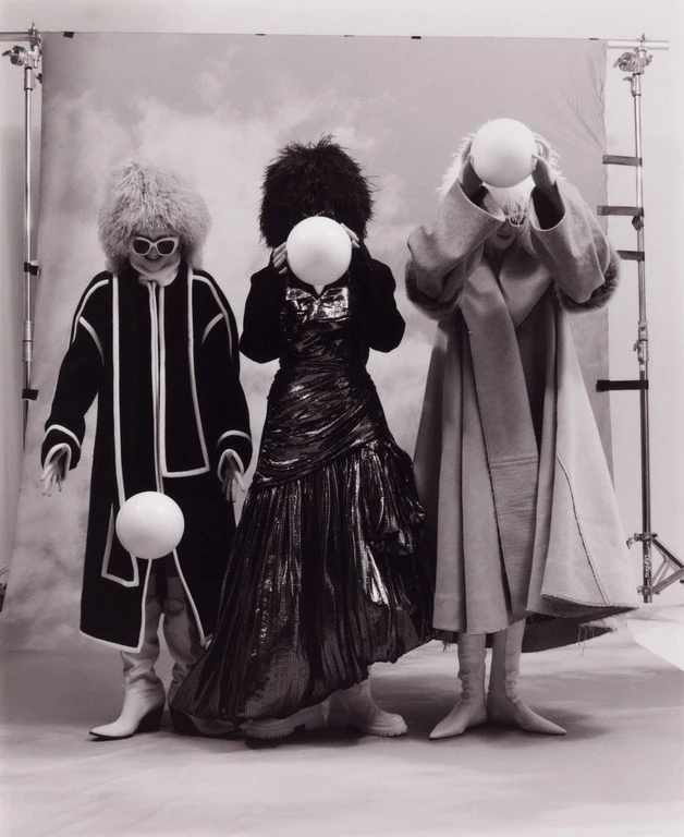 Three models wearing textured hats and coats holding white spherical props in a studio setup by Miguel Bento