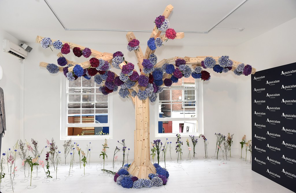 Interior space features an artistic floral installation resembling a tree, constructed from wooden planks and vibrant blue and purple flowers.