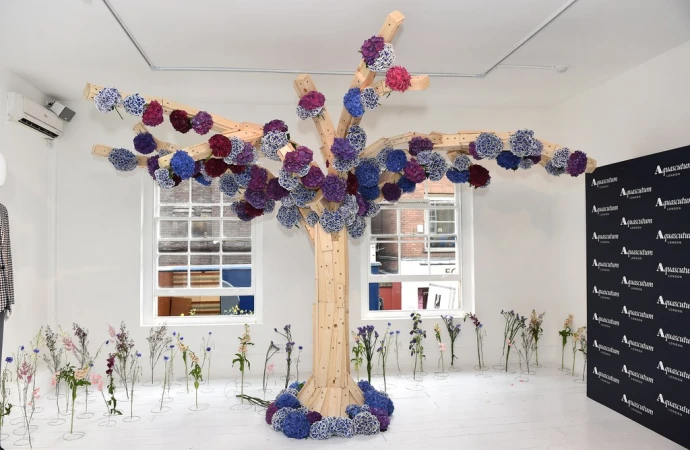 Interior space features an artistic floral installation resembling a tree, constructed from wooden planks and vibrant blue and purple flowers.