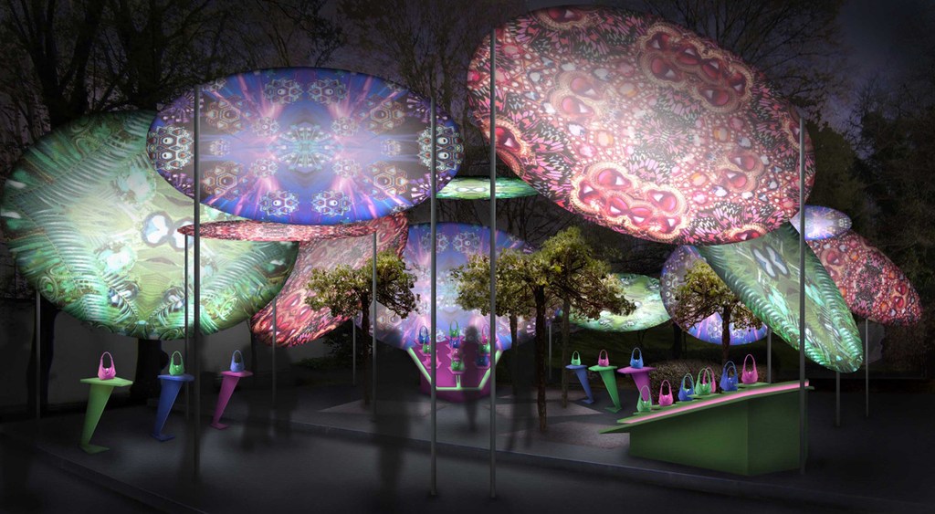 An art installation with large discs displaying patterns, small trees, and handbags displayed on colorful stands, under a dark sky.