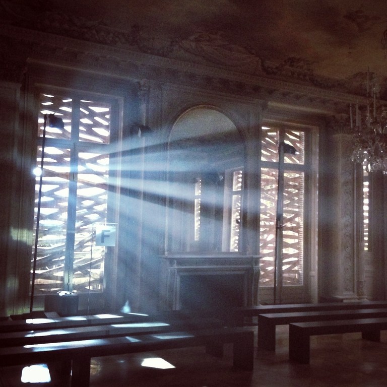 Ornate room interior with sunlight streaming through lattice windows, casting shadows on benches and highlighting architectural details.