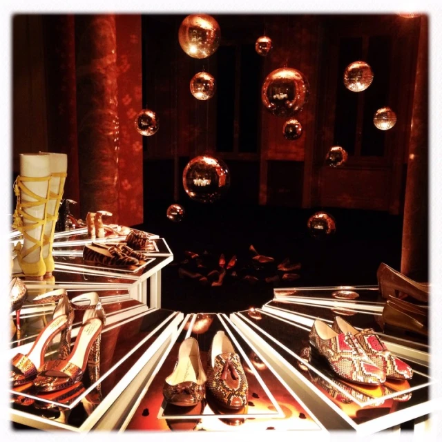 Eye-level shot of a window display featuring various styles of women's shoes on tiered platforms, complemented by hanging disco balls.