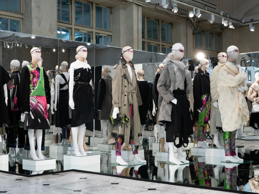 Fashion runway display of mannequins with futuristic face coverings showcasing diverse clothing styles in a bright, minimalist environment.
