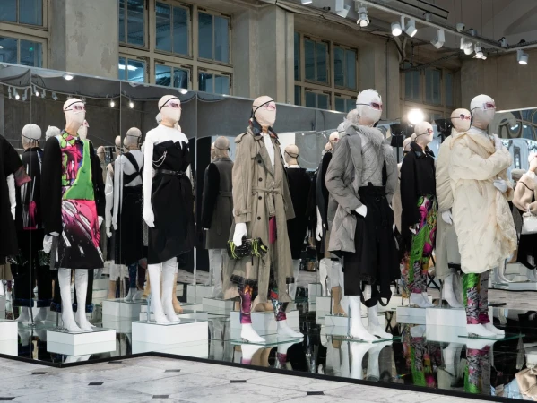 Fashion runway display of mannequins with futuristic face coverings showcasing diverse clothing styles in a bright, minimalist environment.
