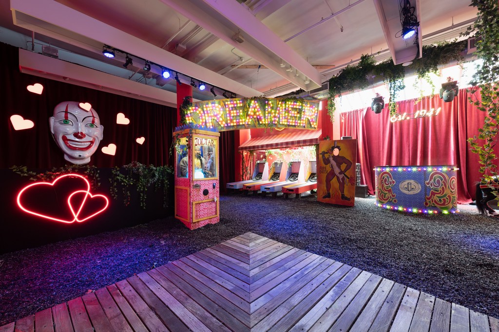 Carnival-themed event space with illuminated signs, vintage games, and decorative clown head, creating a playful and nostalgic atmosphere.