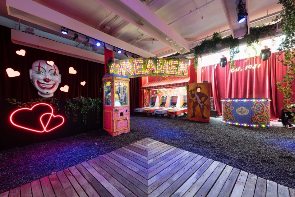 Carnival-themed event space with illuminated signs, vintage games, and decorative clown head, creating a playful and nostalgic atmosphere.