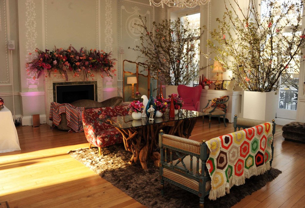 Interior shot features living room furniture, glass-top table with tree-branch base, floral decorations, and flowers on fireplace mantel.
