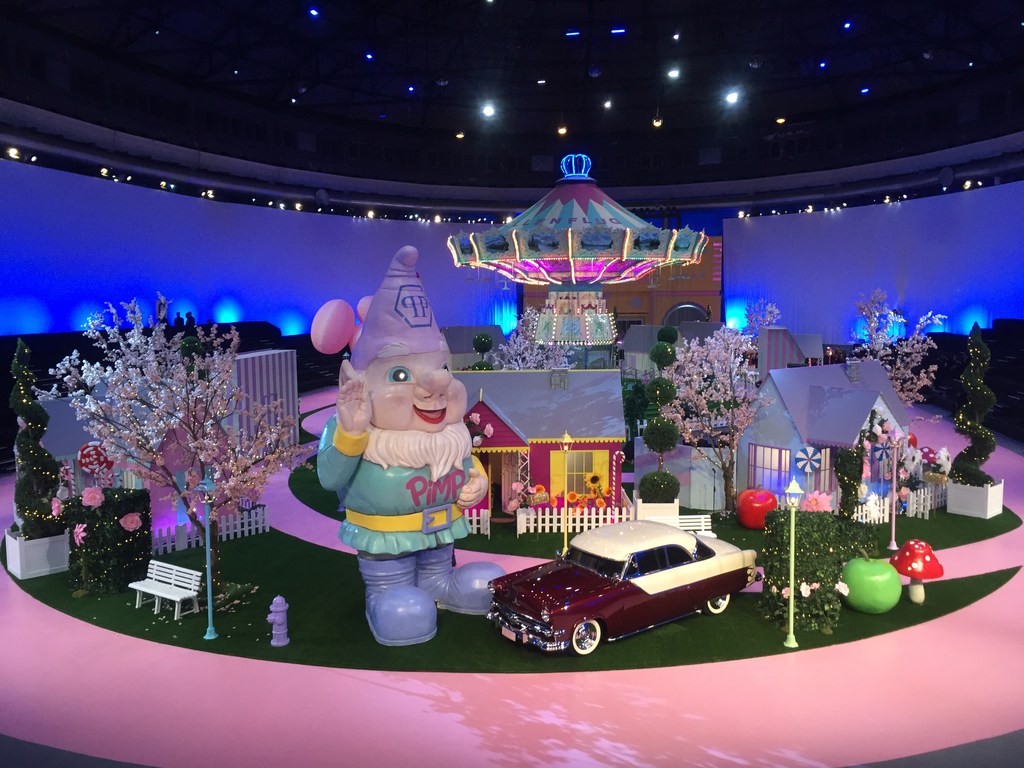 Whimsical scene with gnome statue, vintage car, and carousel against a blue backdrop. Playful, fantasy-themed arrangement.