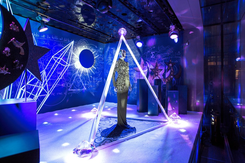 Mannequin in an ornate dress inside a triangular frame in a room with stars, moons, and geometric designs on walls and ceiling.