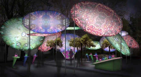Art installation featuring glowing oval patterned canopies and illuminated displays of colorful handbags by Simon Costin