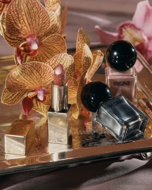 Still life shot of lipstick, nail polish bottles, and orchid flowers on a silver tray, highlighting beauty and elegance in a studio.