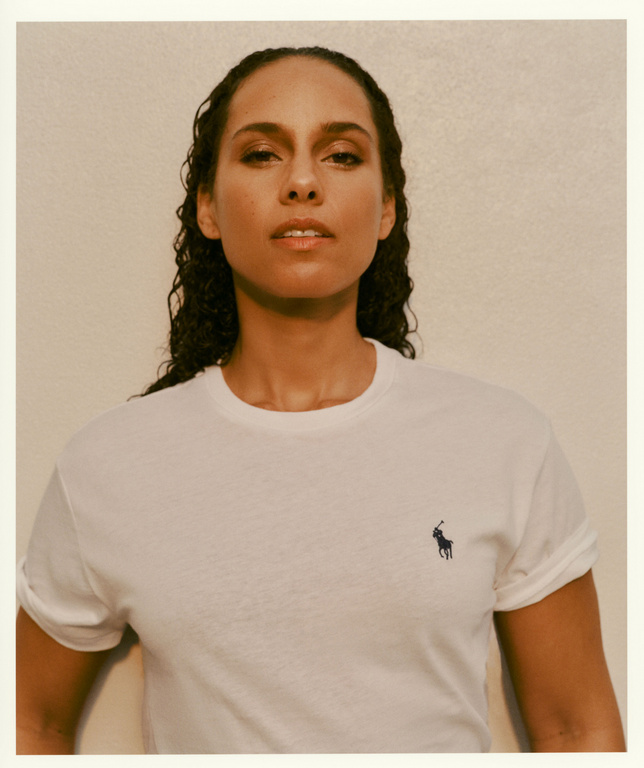 Portrait of Alicia Keys wearing a white t-shirt with a Polo logo, standing against a neutral background in a studio environment.