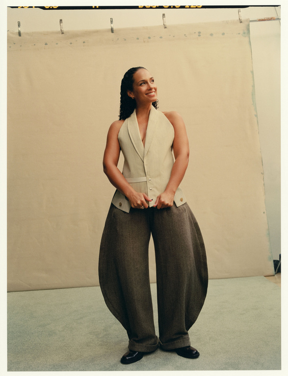 Portrait of smiling woman in halter top and oversized pants in a photo studio with a neutral backdrop, looking off into the distance.
