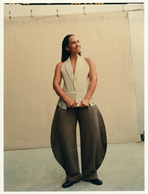 Portrait of smiling woman in halter top and oversized pants in a photo studio with a neutral backdrop, looking off into the distance.