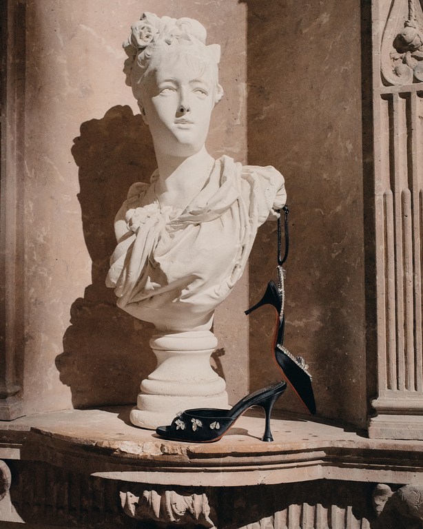 Bust statue with floral headpiece on ledge, displaying two black high-heeled shoes, indoor fashion or art photography.