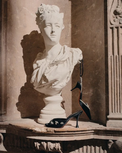 Bust statue with floral headpiece on ledge, displaying two black high-heeled shoes, indoor fashion or art photography. 