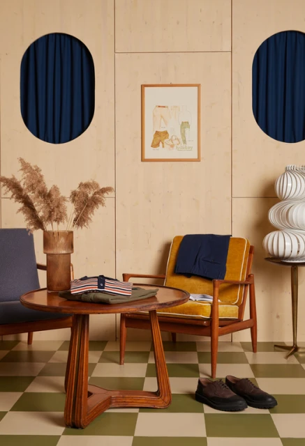 Interior shot featuring a round wooden table, two chairs, and various home decor items set against a paneled wall with blue curtains.