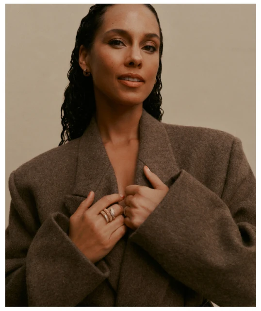 Close-up studio portrait of Alicia Keys wearing a brown wool coat. Keys has long dark hair and is looking at the camera.