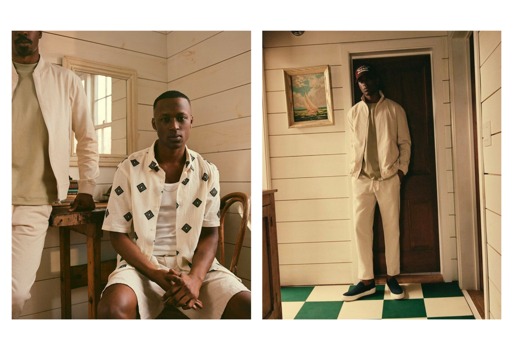 Two African-American men model light-colored jackets, shirts, and pants in a bright, traditionally styled interior with white wood paneling.
