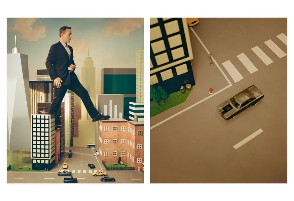 A man in a suit strides confidently across miniature city skyscrapers, next to a detailed model car and street scene under studio lighting.
