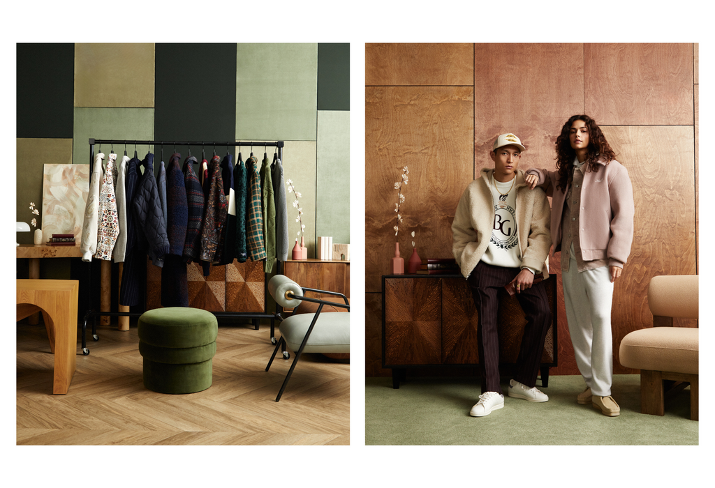 Two people model clothing in an interior setting with warm wood paneling and modern decor; clothing rack and furniture visible.