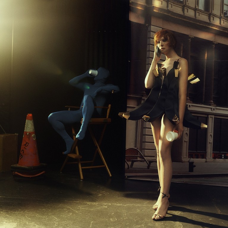 A fashion photo features a red-haired model on a phone, and a blue-suited figure drinking in the background, against an urban backdrop.