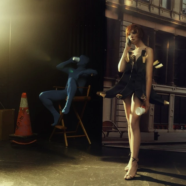 A fashion photo features a red-haired model on a phone, and a blue-suited figure drinking in the background, against an urban backdrop.